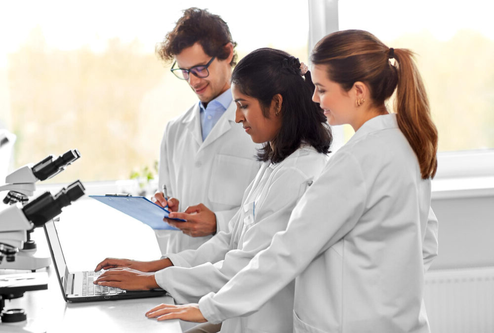 Three cancer researchers in lab coats collaborating on a funding application for innovative cancer immunotherapy research in Canada.