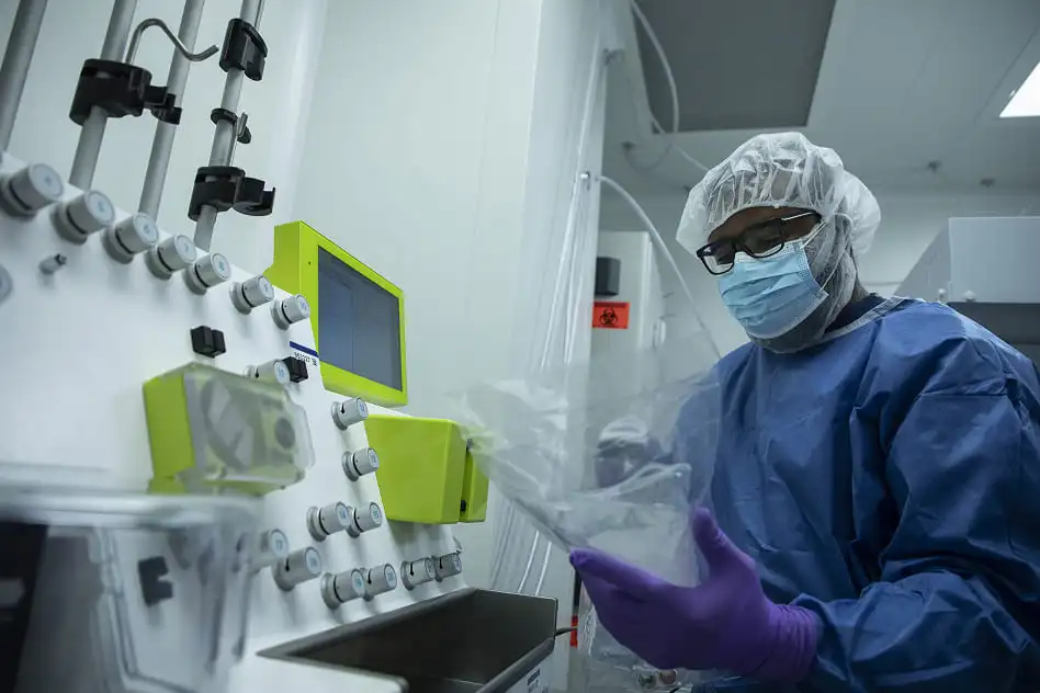 Researcher wearing protective gear and mask operates specialized equipment in a cleanroom environment for cell therapy manufacturing and biotherapeutics production.