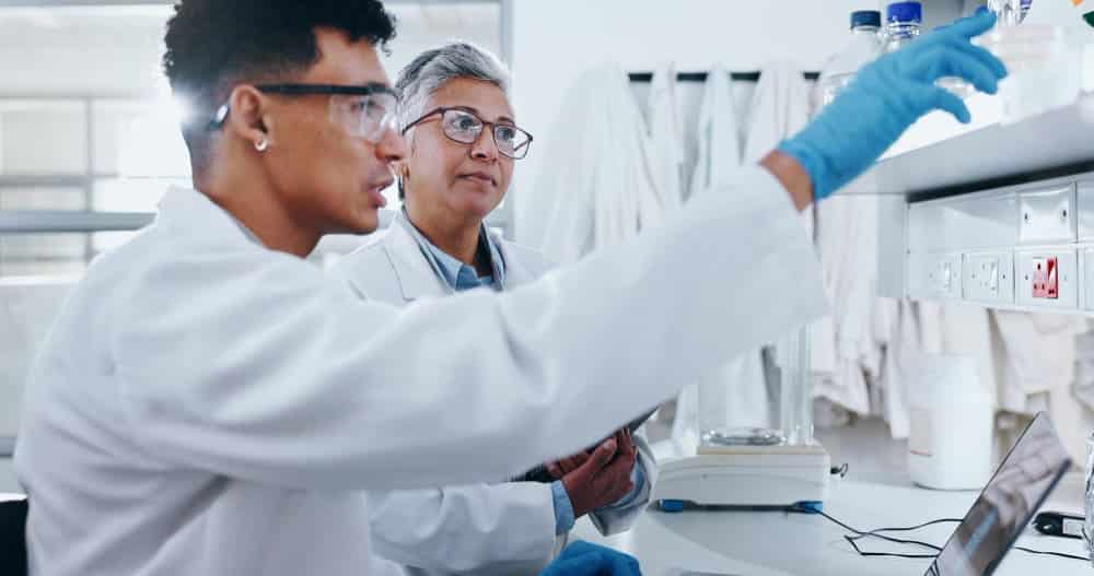 Two scientists in lab coats work together in a laboratory, examining samples and data related to cell therapy process development.
